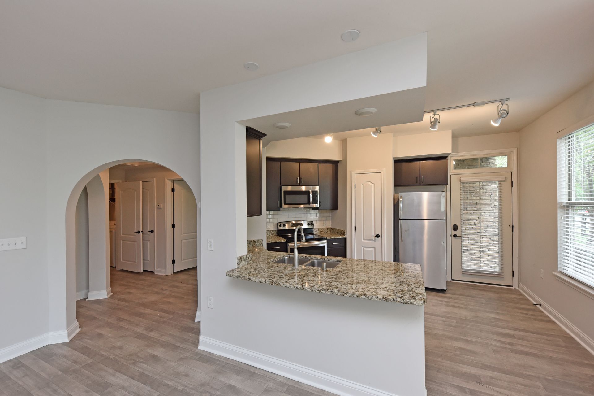 Open-concept kitchen with granite countertops and stainless steel appliances; wooden floors and archway.