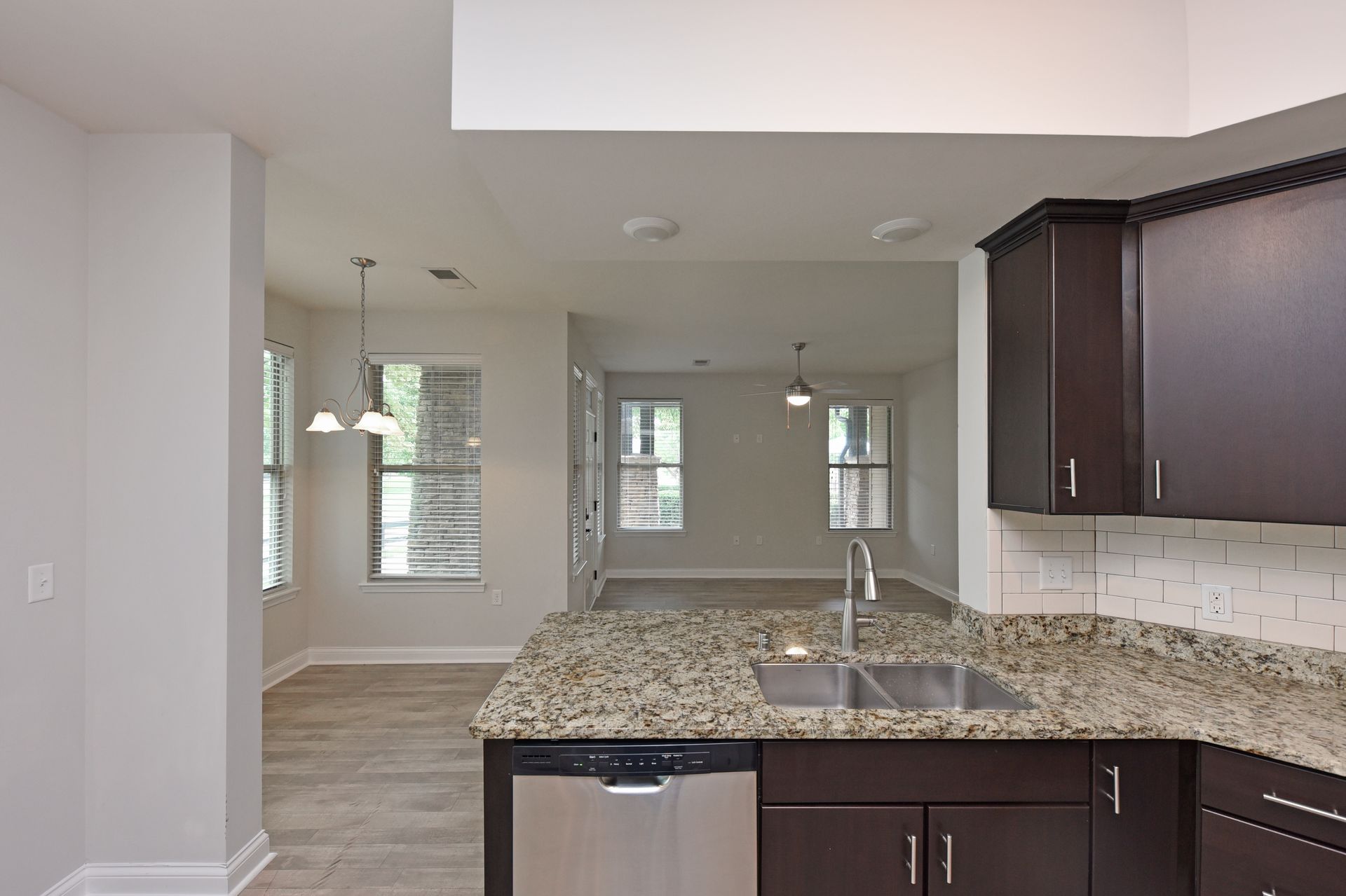 Kitchen with granite countertop, stainless steel sink/dishwasher, dark cabinets, and view into living room.