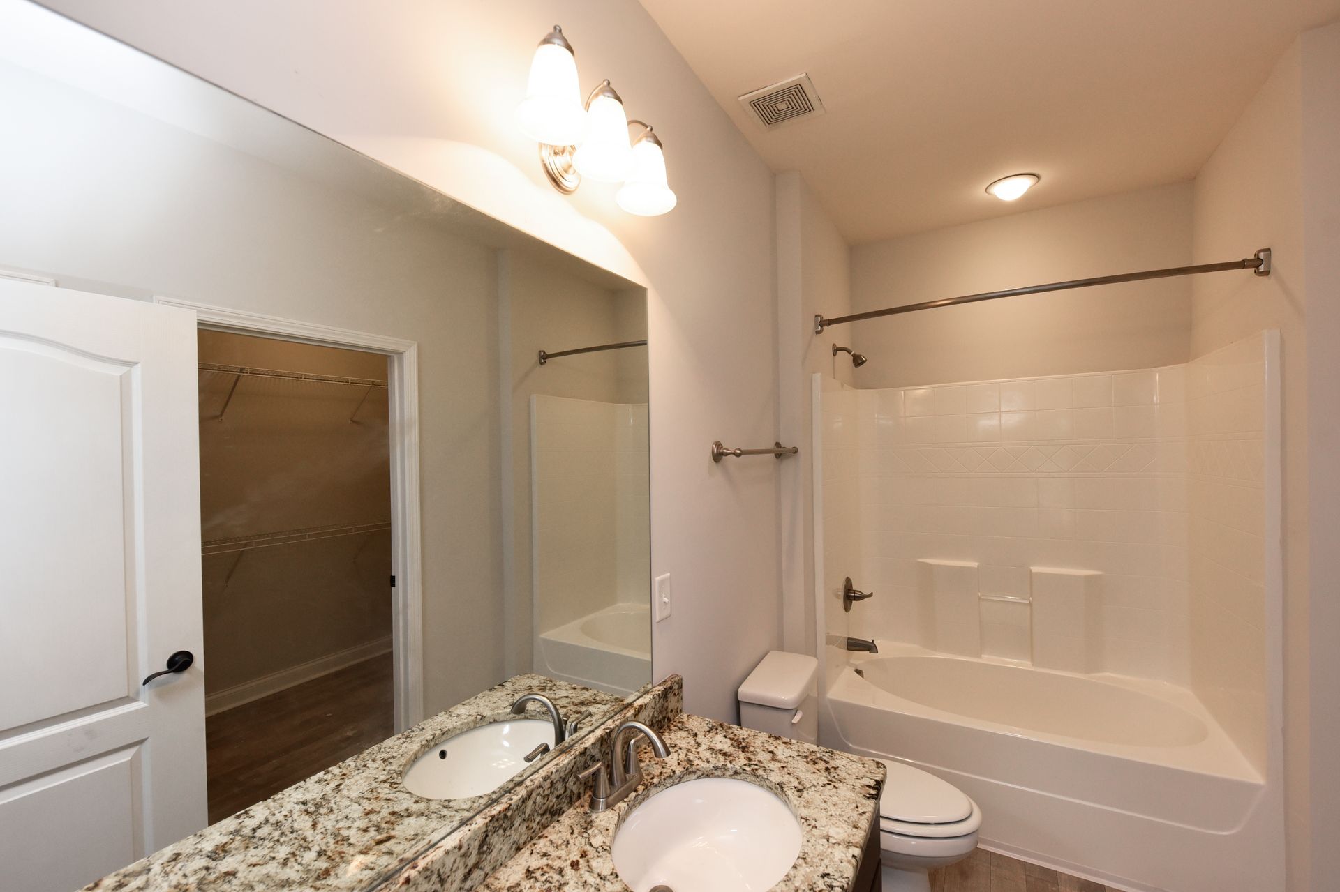 Bathroom with a large mirror, double vanity with granite countertop, and a white bathtub.