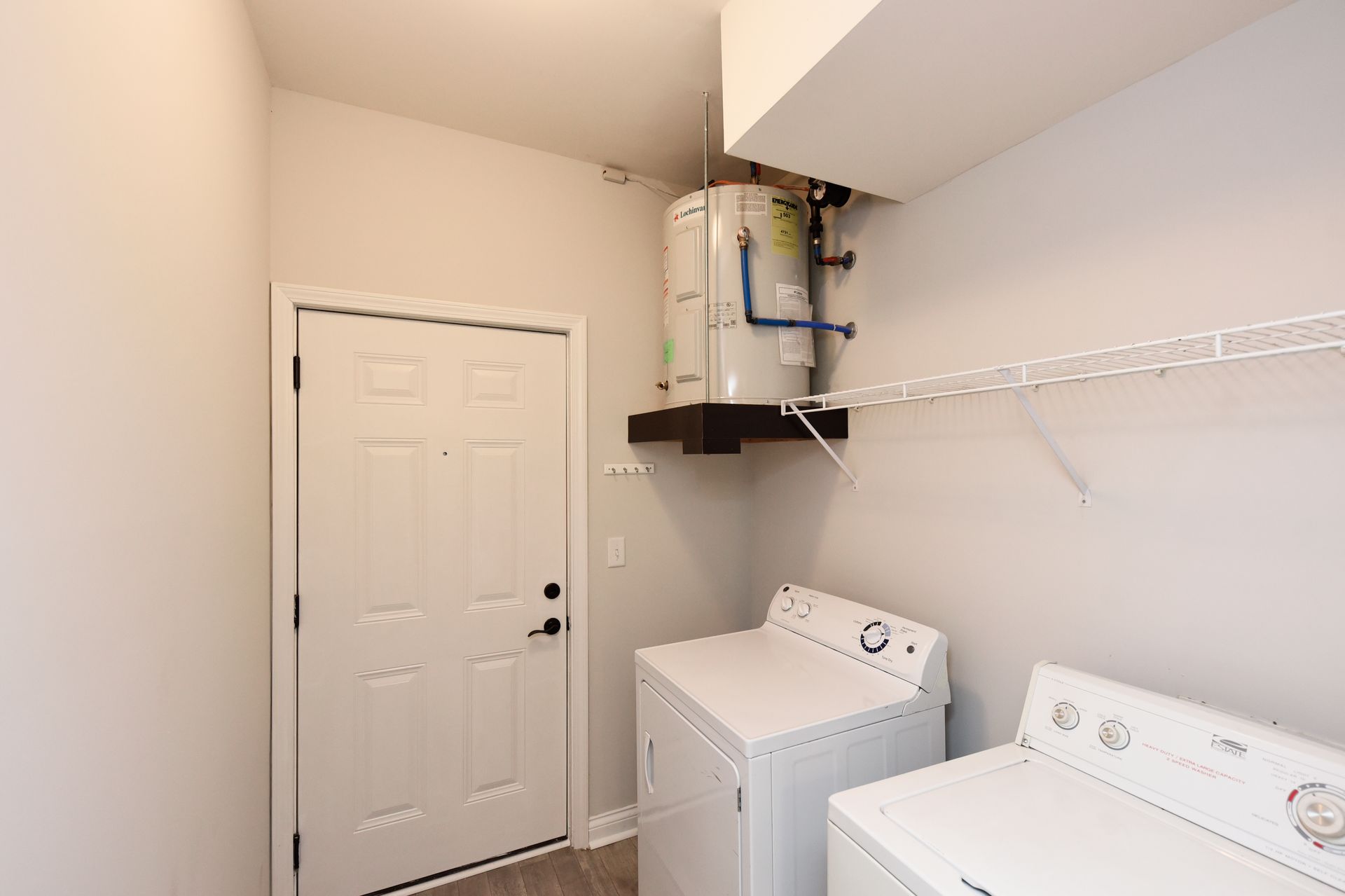 Laundry room with washing machine, dryer, water heater, door, and shelf.