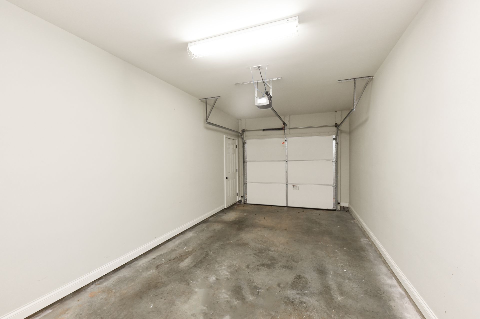 Empty, white garage with a concrete floor, closed garage door, and overhead light.