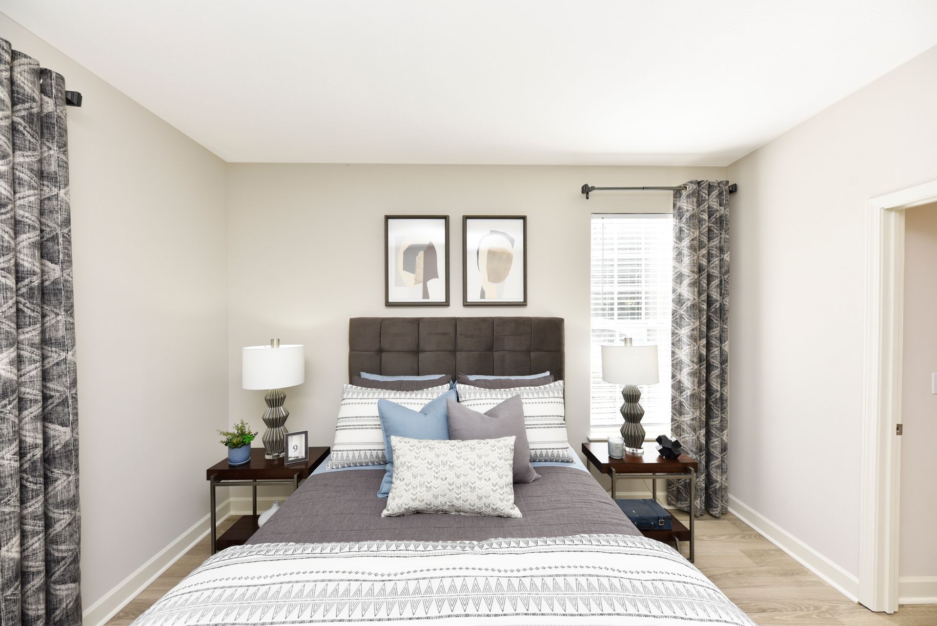 Bedroom with gray and blue bedding, dark furniture, and patterned curtains.