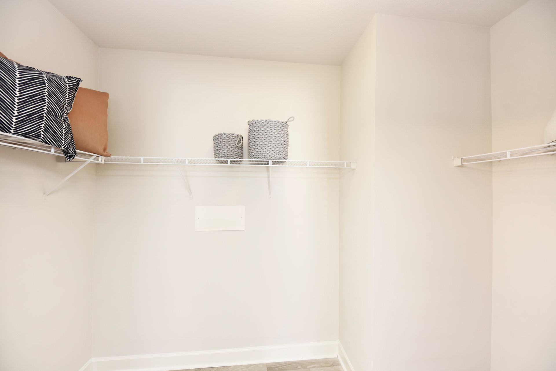 Empty closet with wire shelves, two baskets, and a patterned pillow.