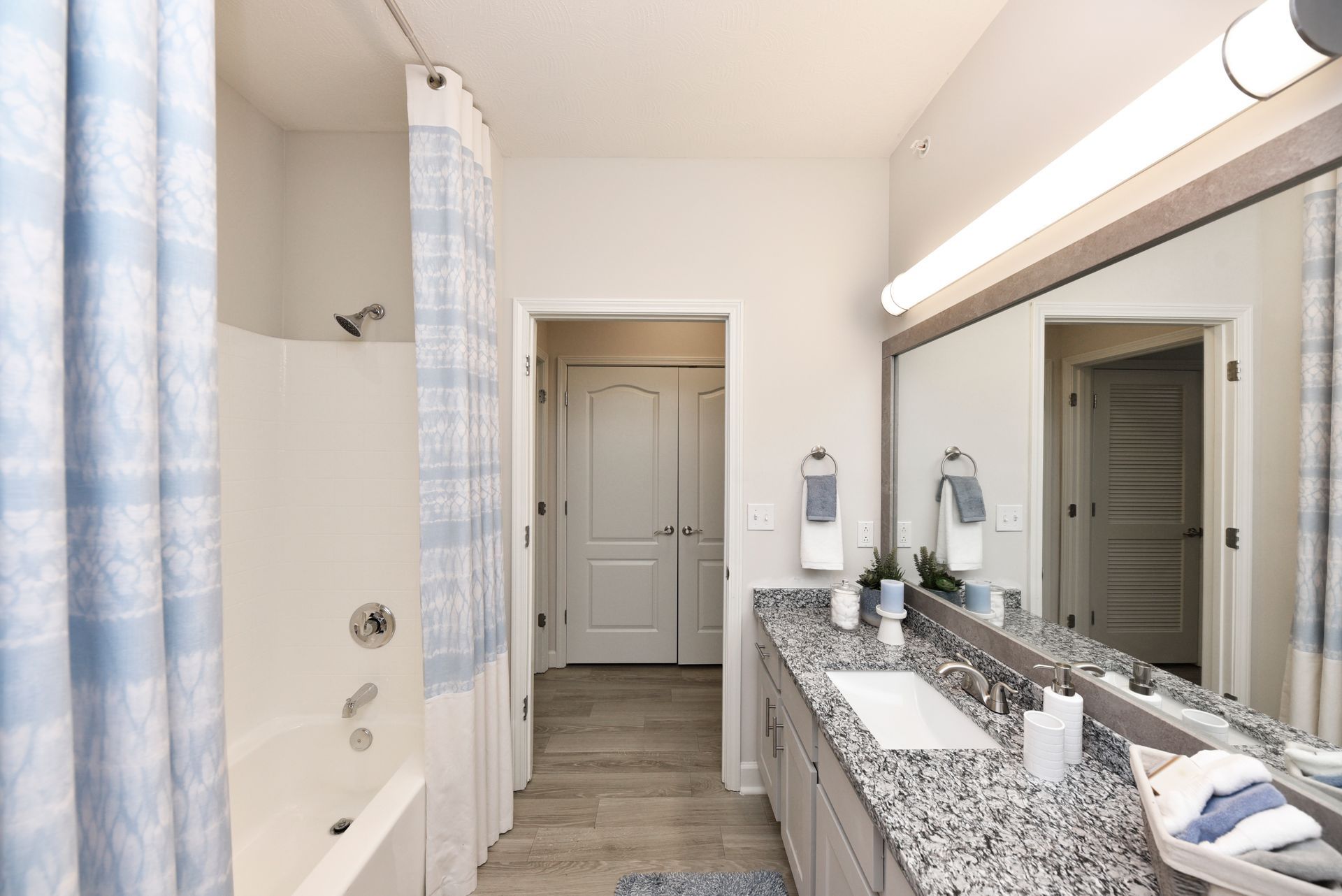 Bathroom with tub, shower, double vanity, and doorway. Gray granite countertop, light blue and white decor.
