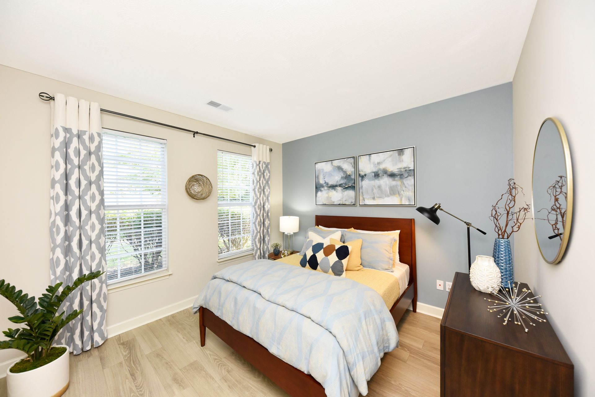 Bedroom with blue and yellow accents, two windows, wooden bed, dresser, and decorative items.
