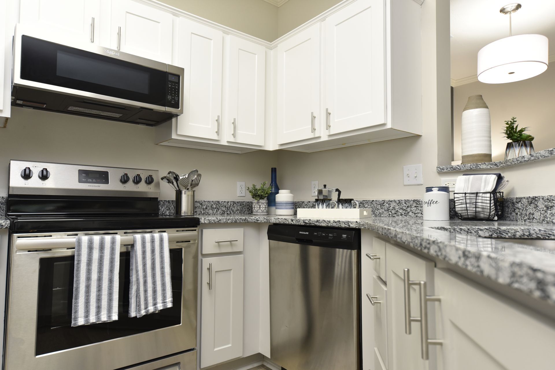 White kitchen with stainless steel appliances, granite countertops, and overhead cabinets.