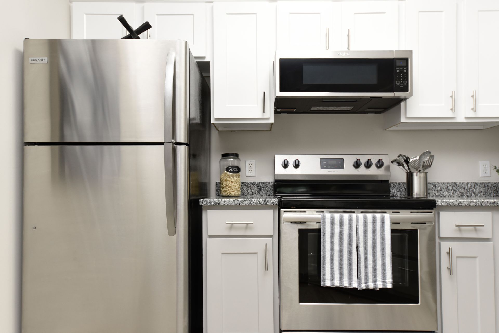 Stainless steel kitchen with white cabinets, microwave above the stove, and a striped towel.
