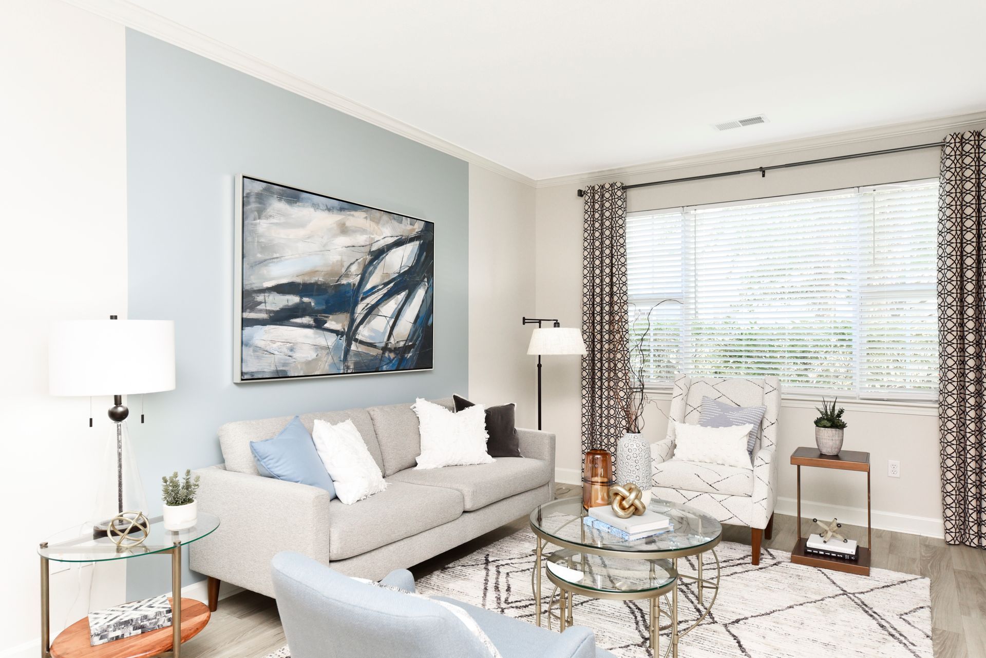 Living room with blue accent wall, gray couch, abstract art, and large window with patterned curtains.