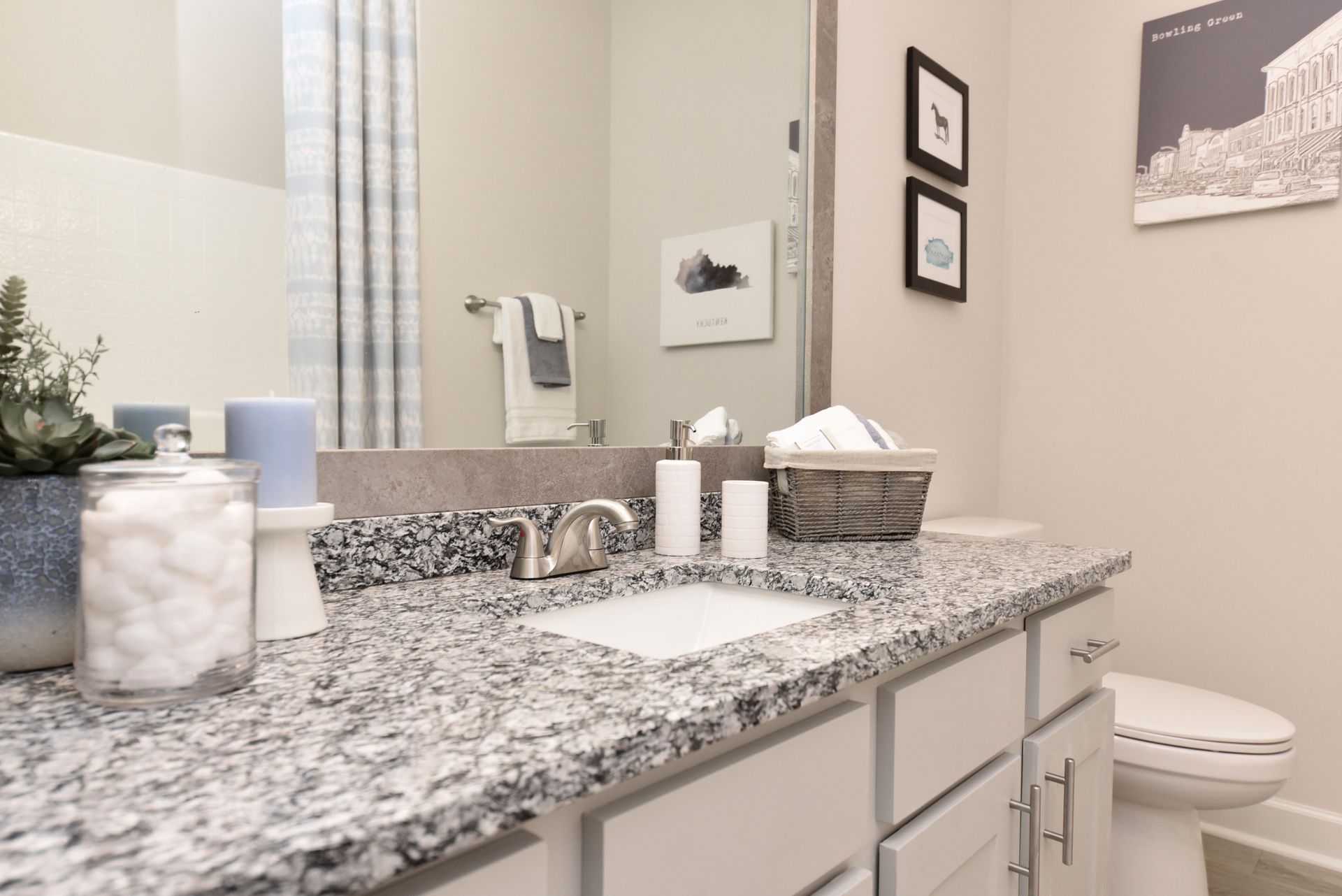Bathroom with granite countertop, white cabinets, mirror, and decorative items.