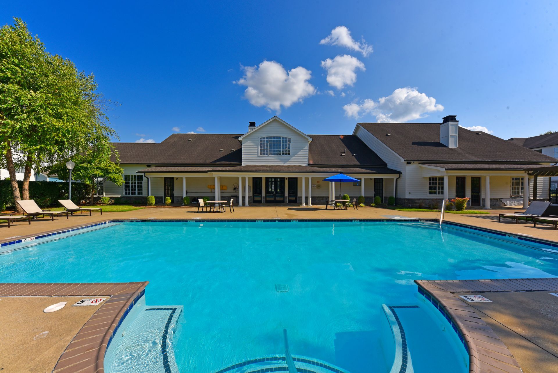 Swimming pool in front of a white building with a porch under a blue sky with clouds.