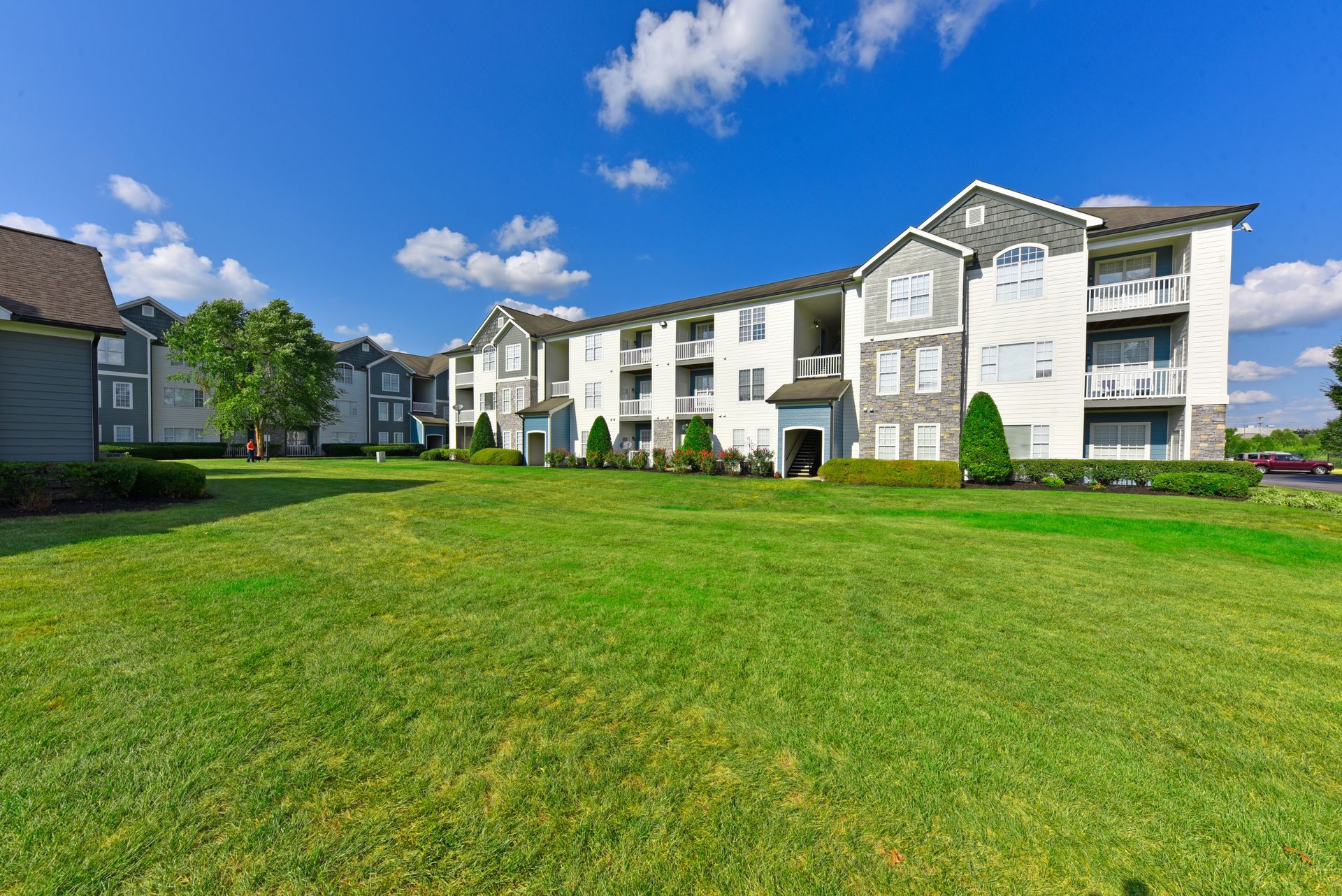 Apartment building with white and grey facade and green lawn under a blue sky with clouds.