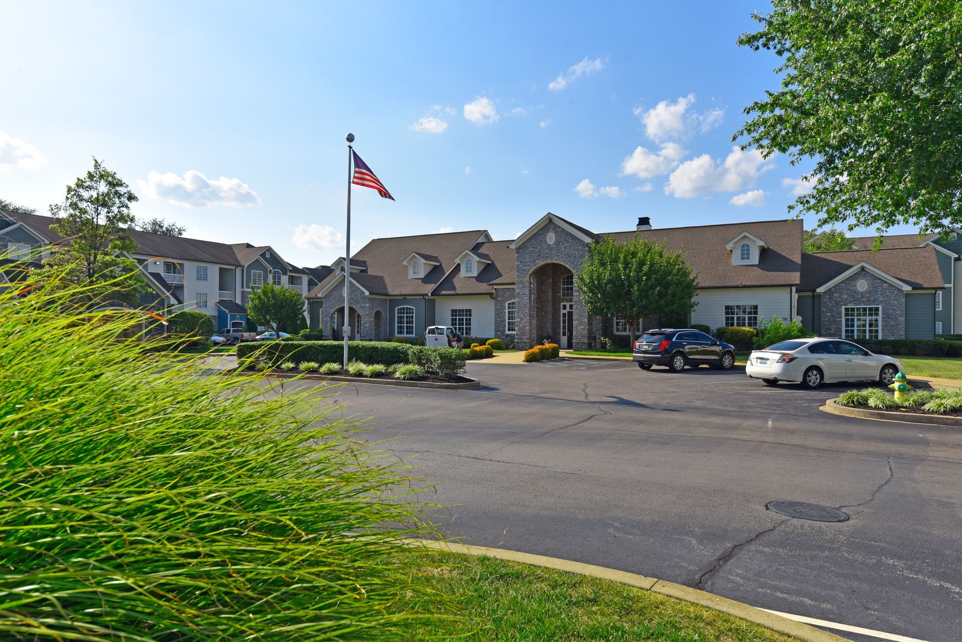 Apartment complex with American flag waving in the wind. Cars parked in front. Blue sky.