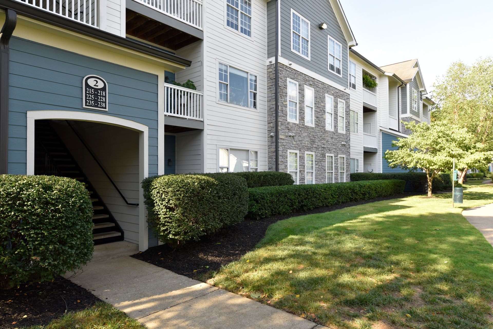 Apartment complex exterior with green lawn, bushes, and blue and gray siding.
