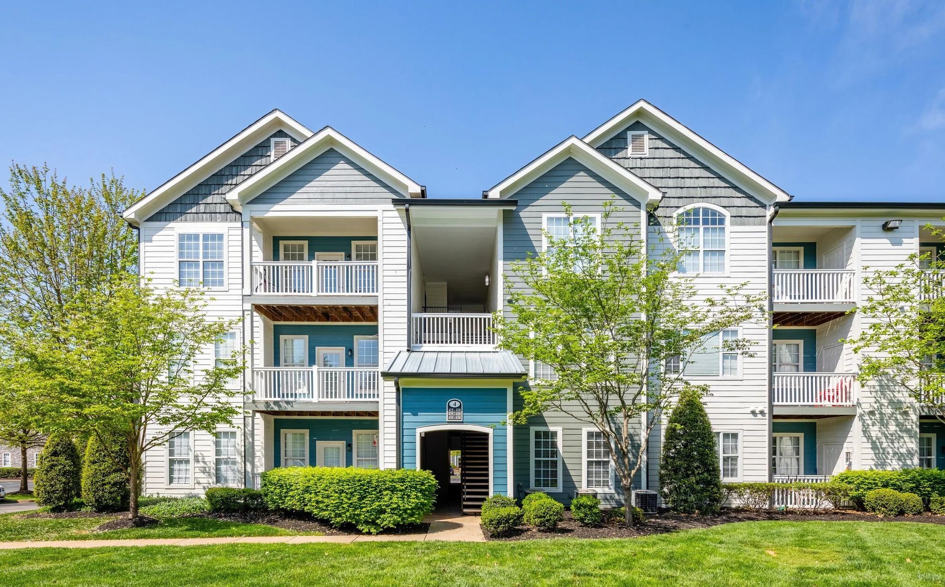 Apartment building exterior, light blue and white with balconies, green lawn and blue sky.