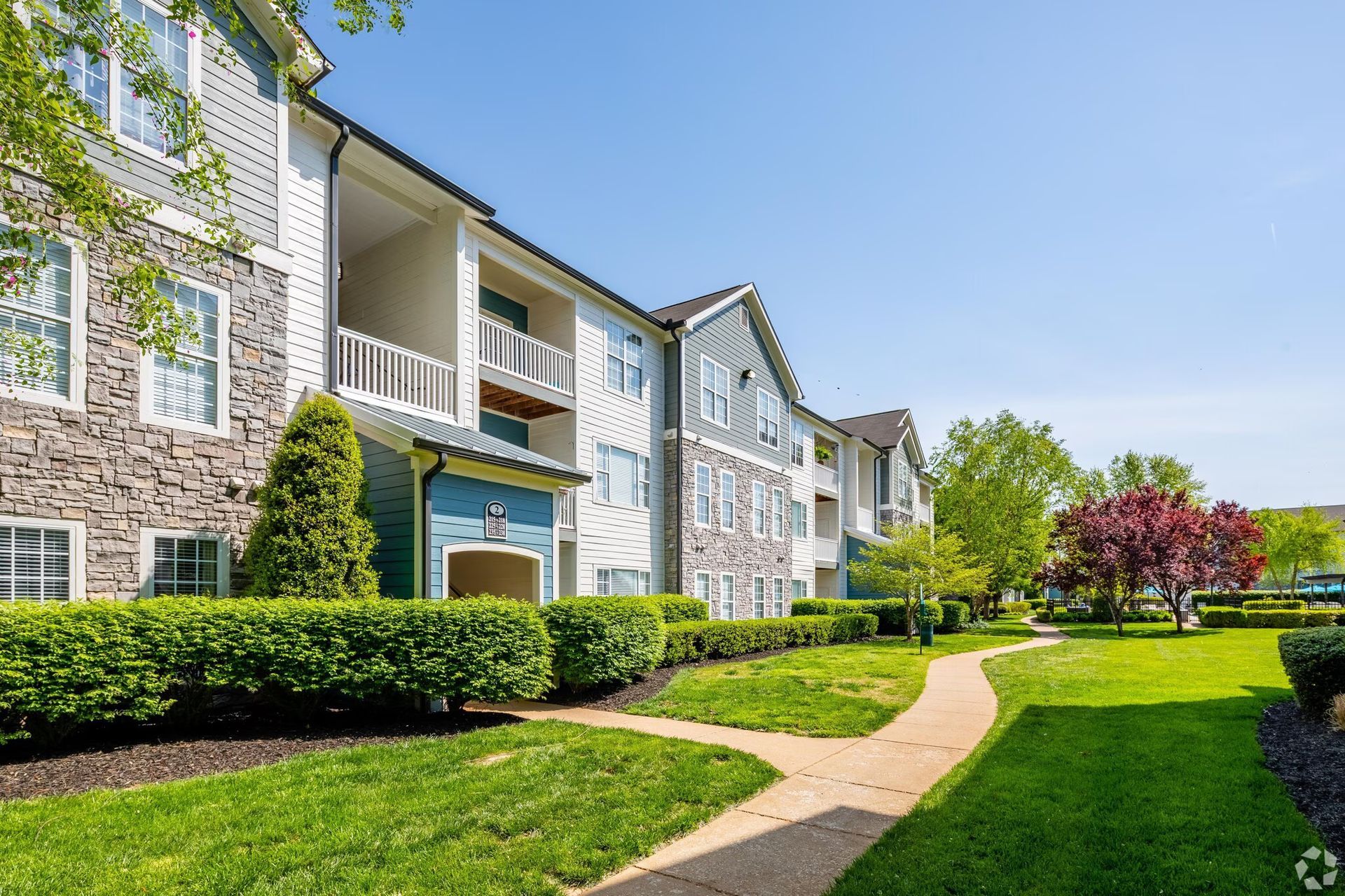 Apartment building exterior with green lawns, a pathway, and a blue sky.