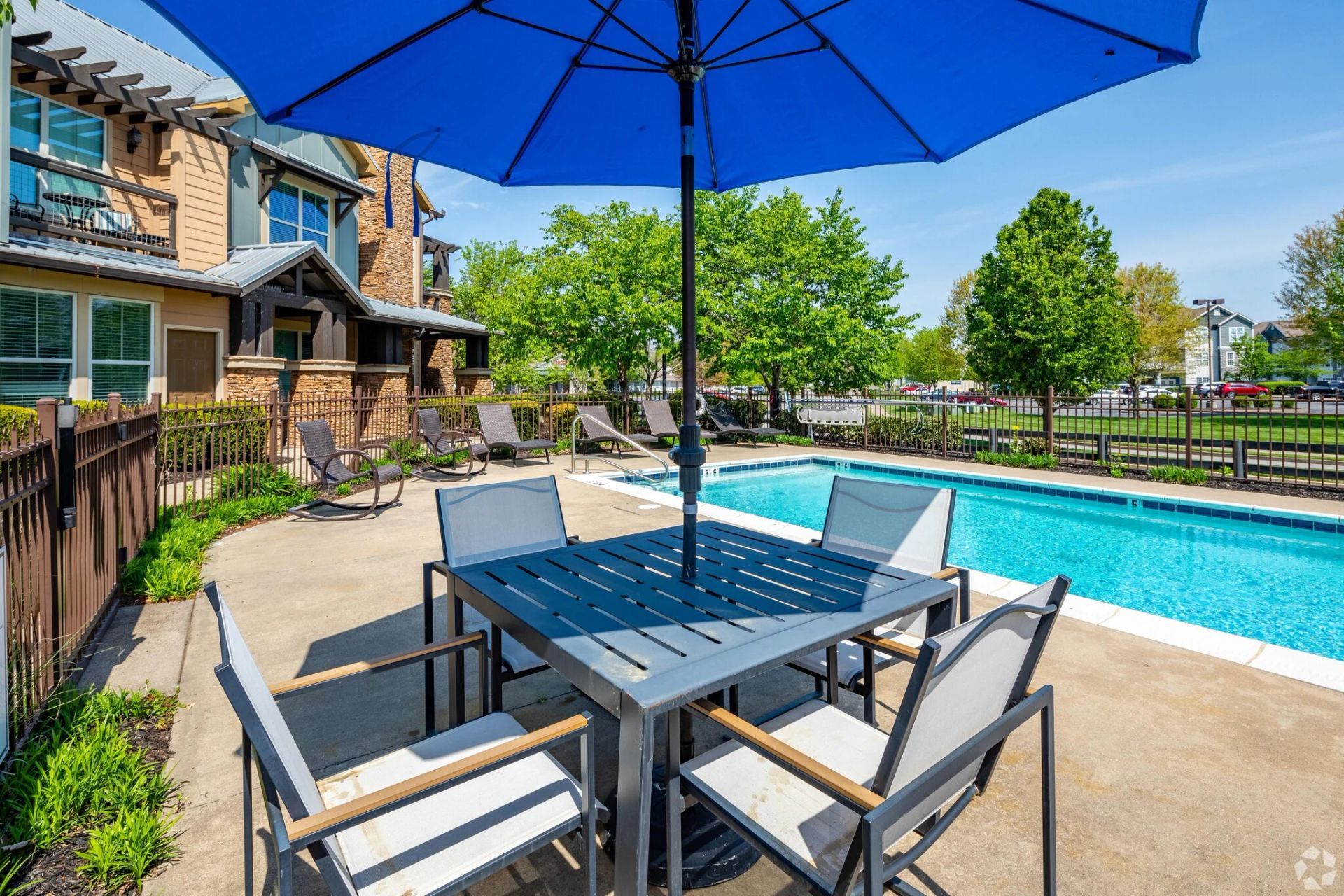 Outdoor pool with a blue umbrella shading a gray table and chairs.