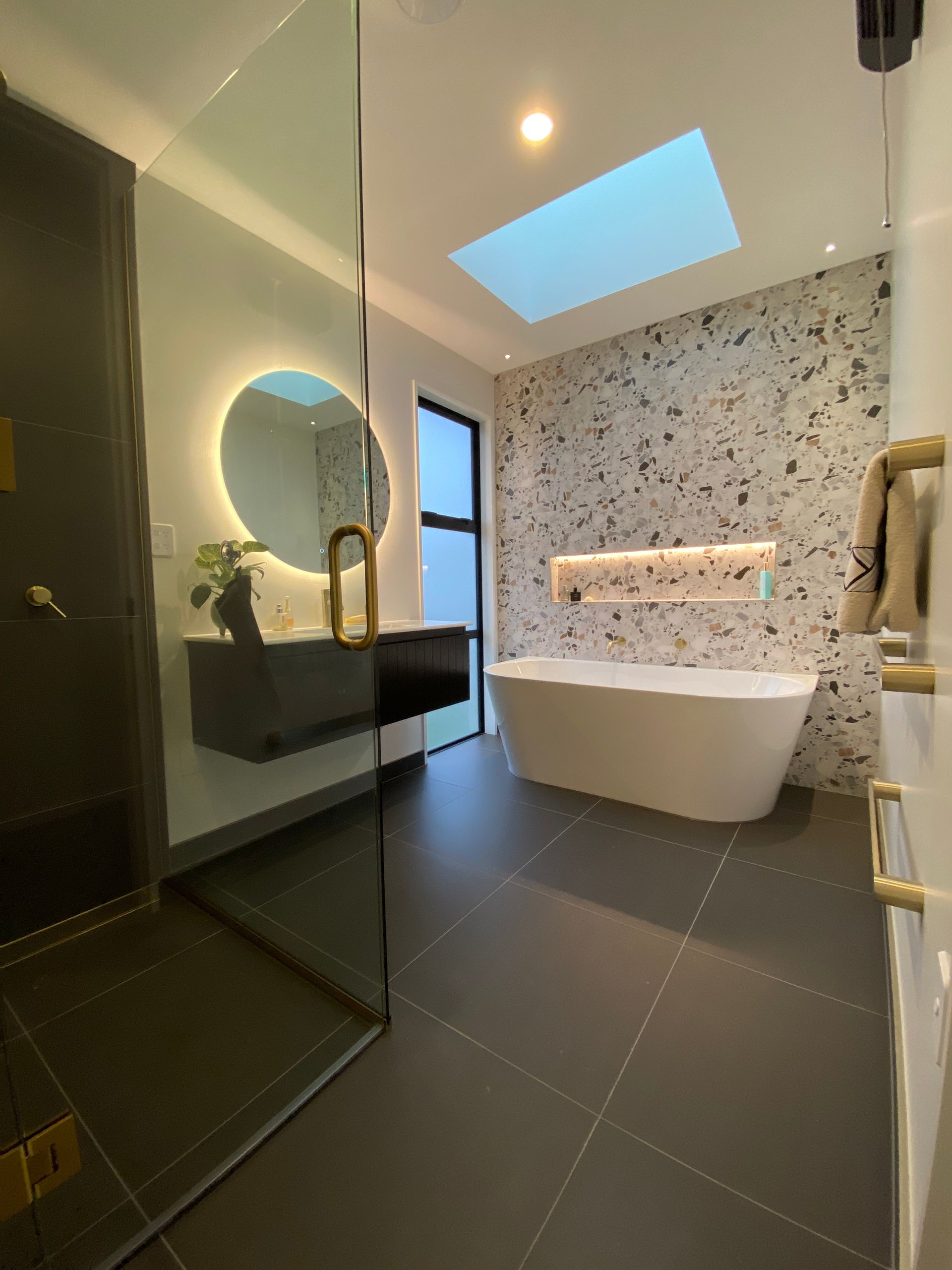A bathroom with a bathtub , sink , mirror and skylight.