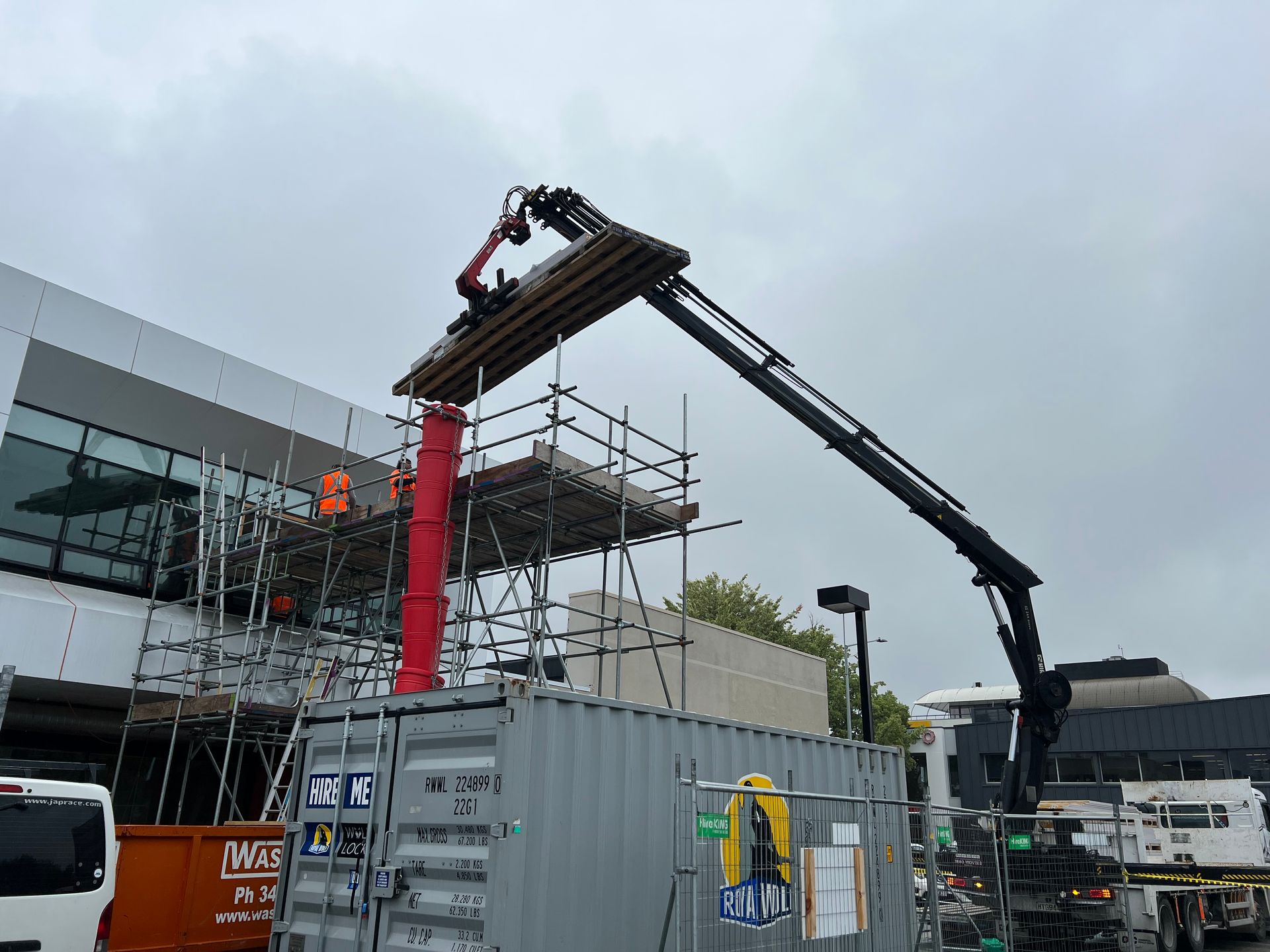 A crane is lifting a large piece of wood over a shipping container.