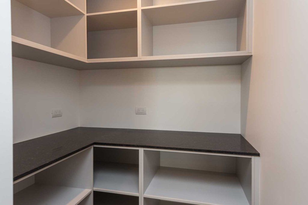 An empty walk in closet with lots of shelves and a black counter top.