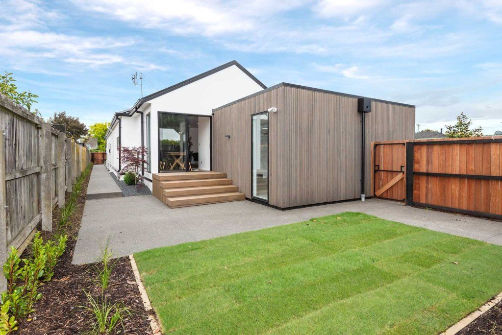 The backyard of a house with a large lawn and a wooden fence.
