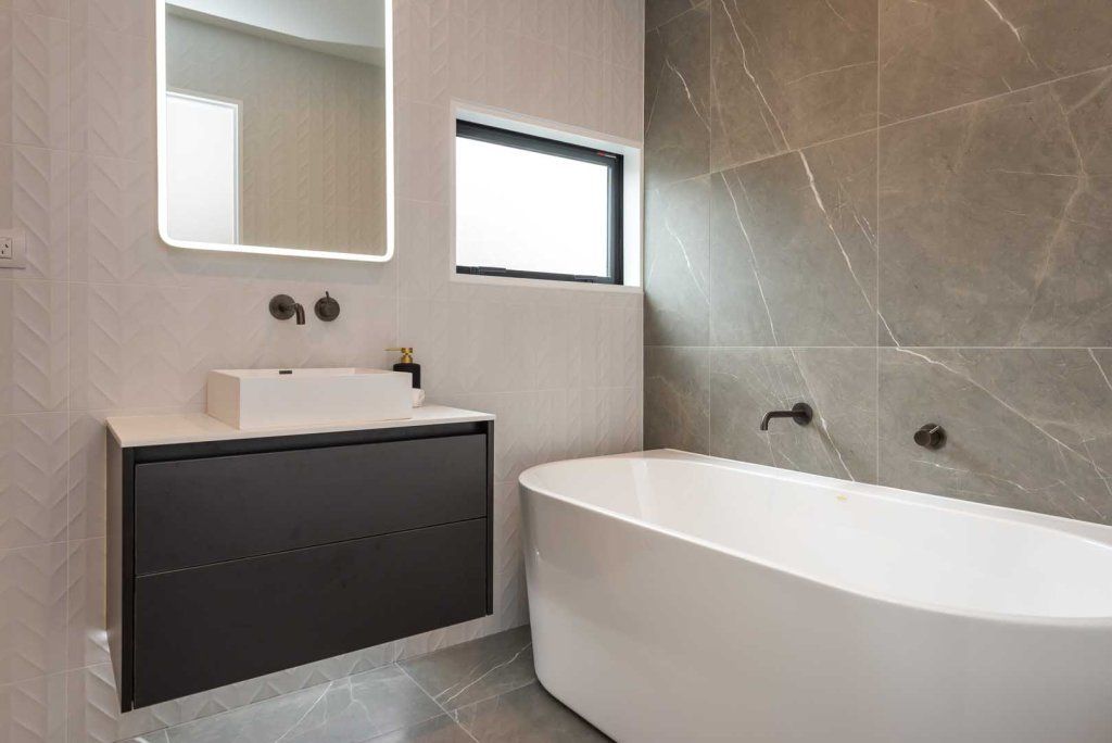 A bathroom with a bathtub , sink , mirror and window.