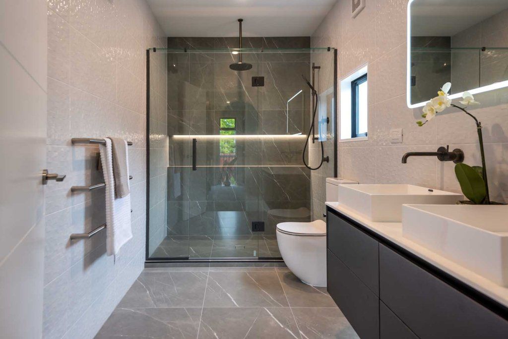A bathroom with a walk in shower , toilet , sink and mirror.