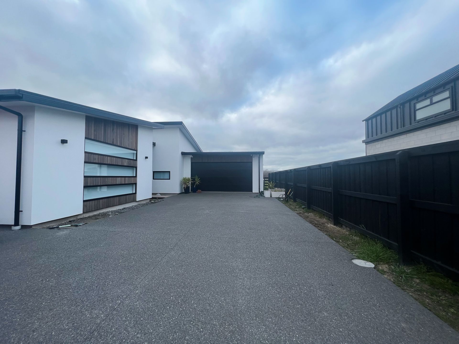 A driveway leading to a house with a garage and a black fence.