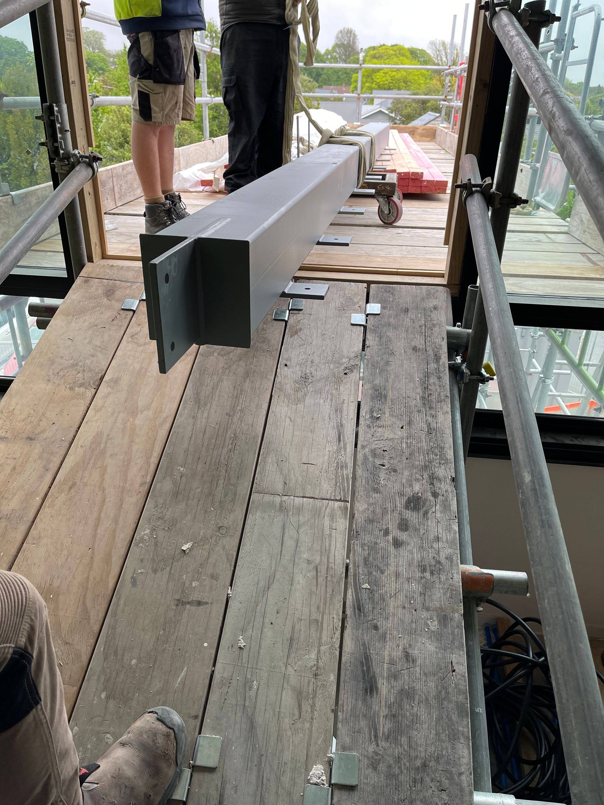 A man is standing on a wooden scaffolding holding a metal beam.
