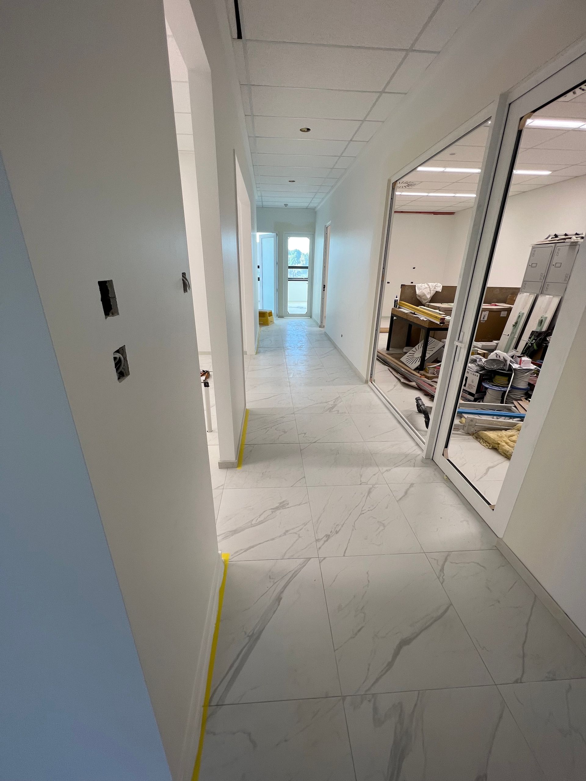 A long hallway with white walls and marble floors in a building under construction.