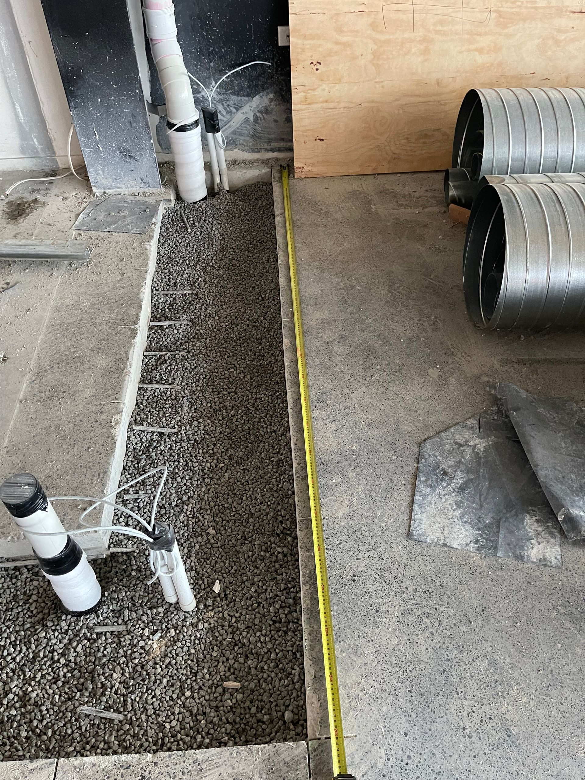 A measuring tape is laying on the floor next to a pipe.