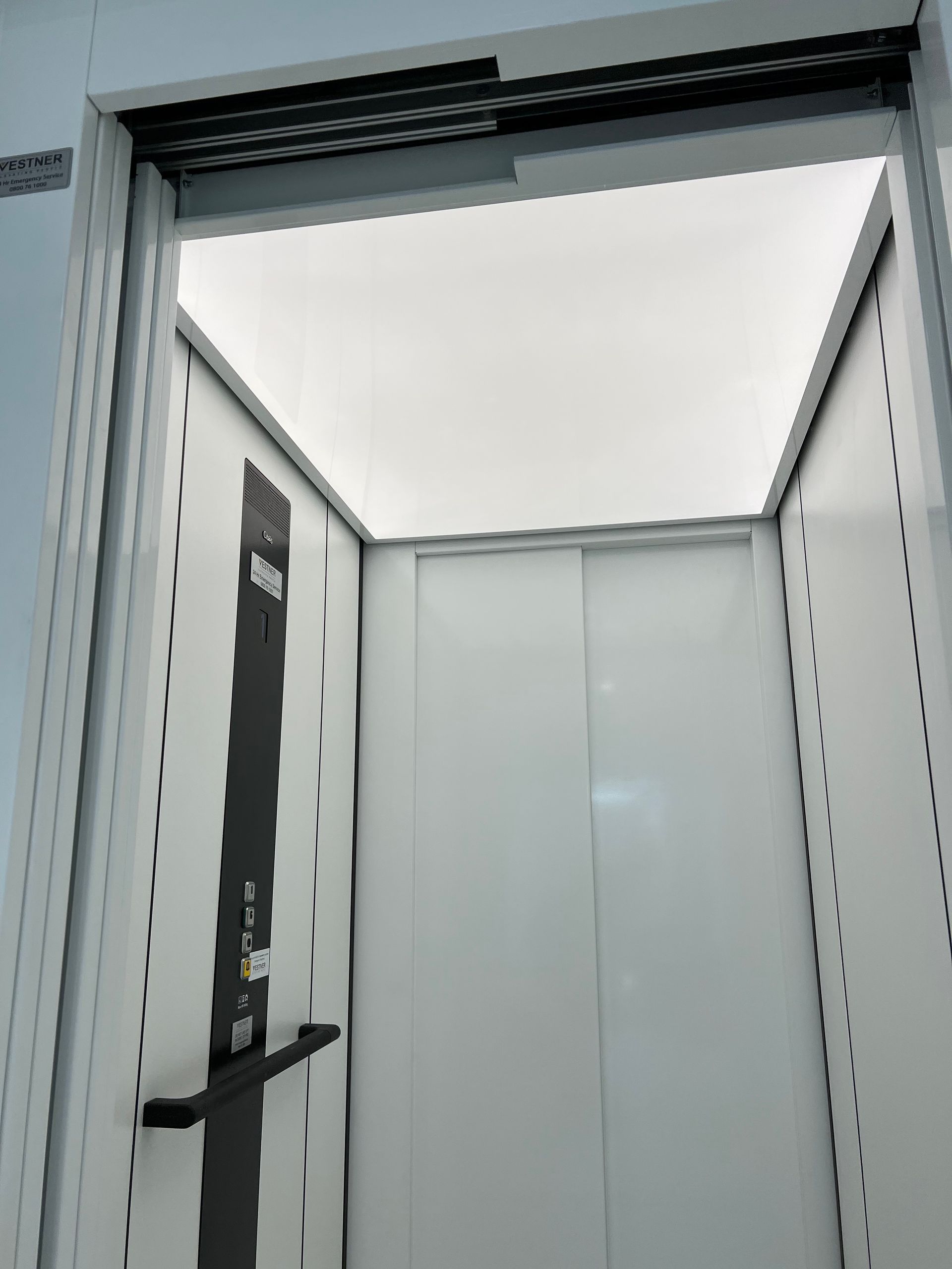A white elevator with a black door and a white ceiling