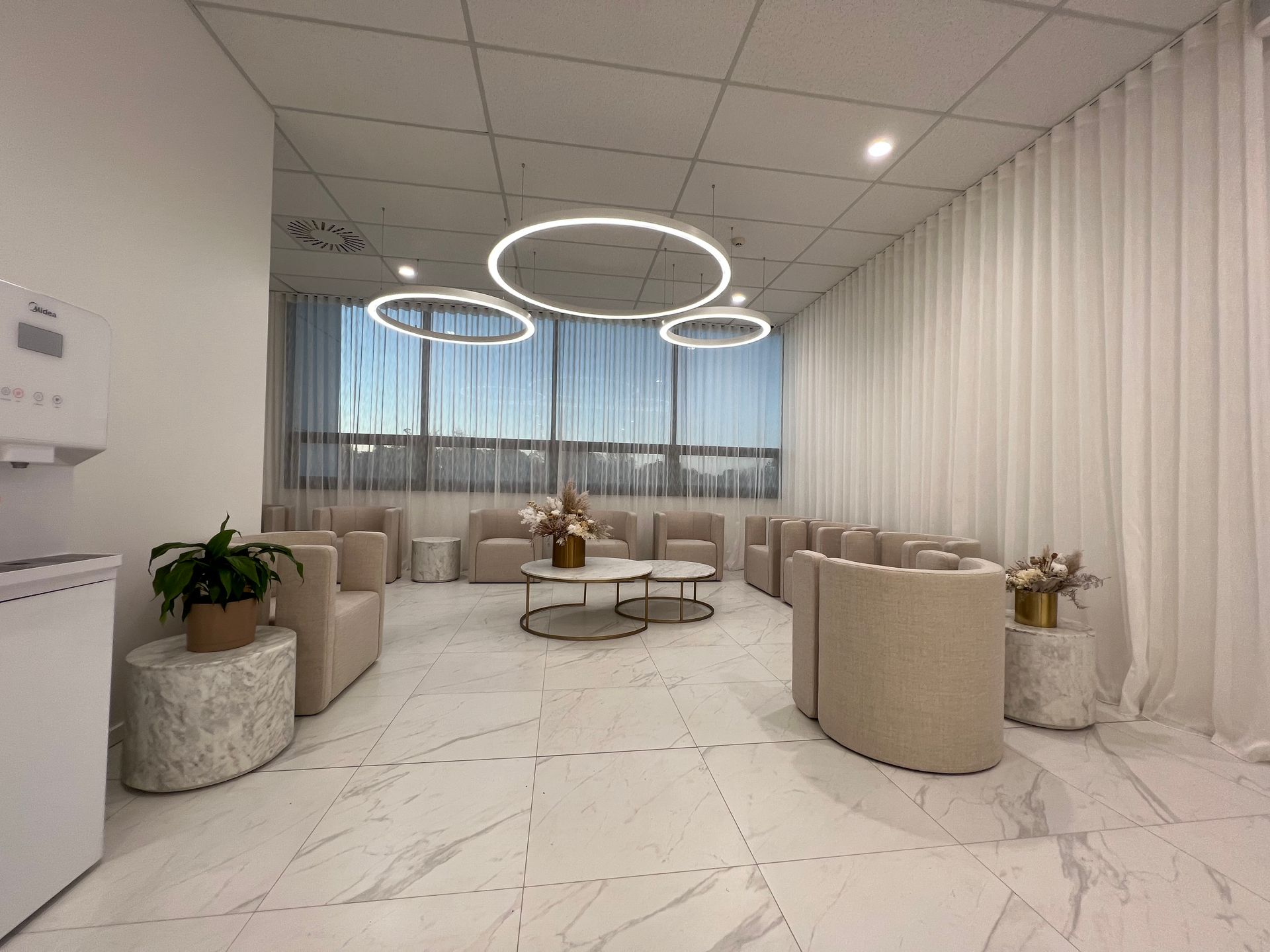 A waiting room with chairs , tables and a water dispenser.
