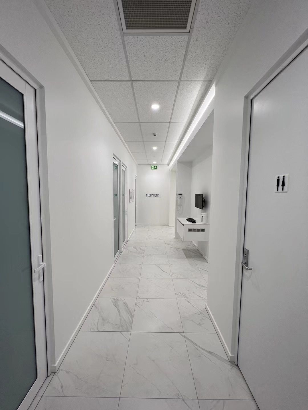 A long hallway with white walls and tile floors in a hospital.