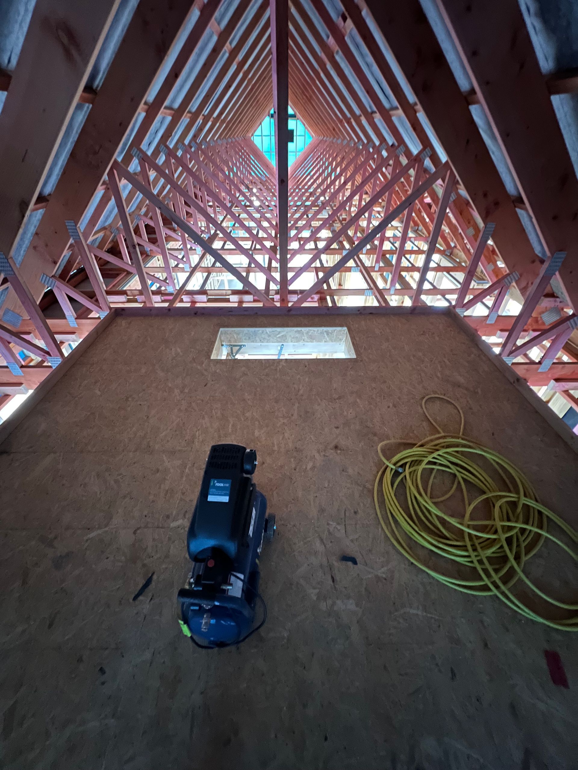 An air compressor is sitting in the attic of a building under construction.