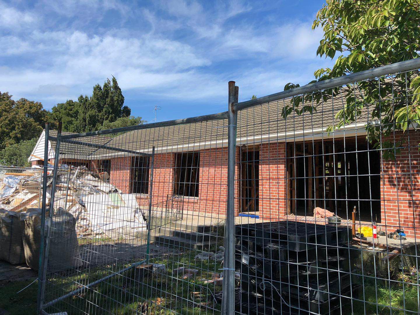 A brick house is being demolished and is behind a fence.