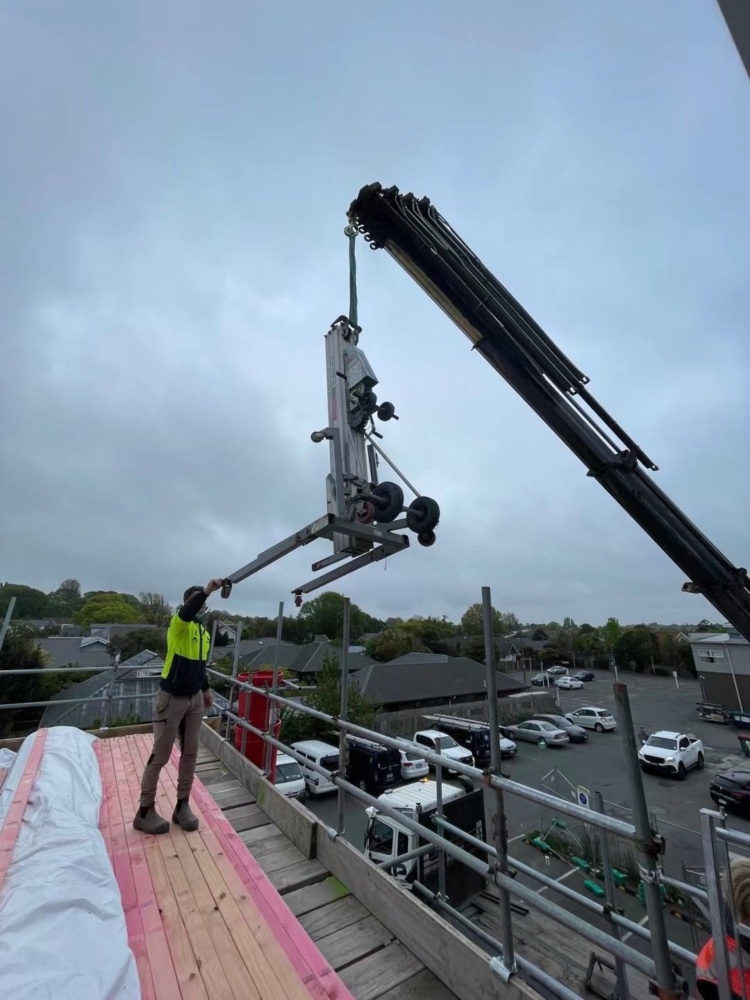 A man is standing on top of a roof next to a crane.