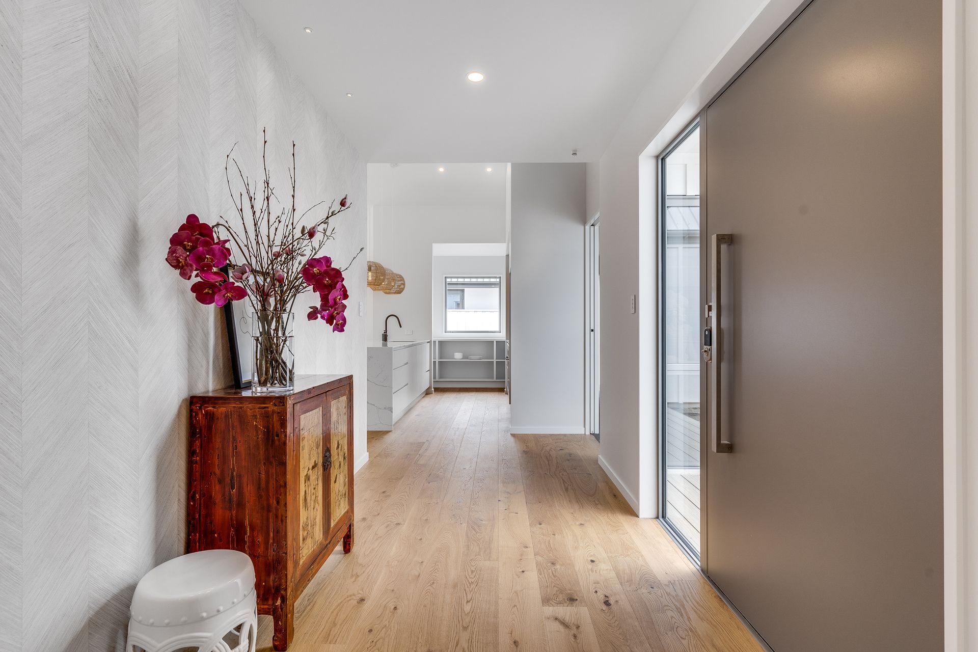 A hallway with hardwood floors , a wooden cabinet and a vase of flowers.