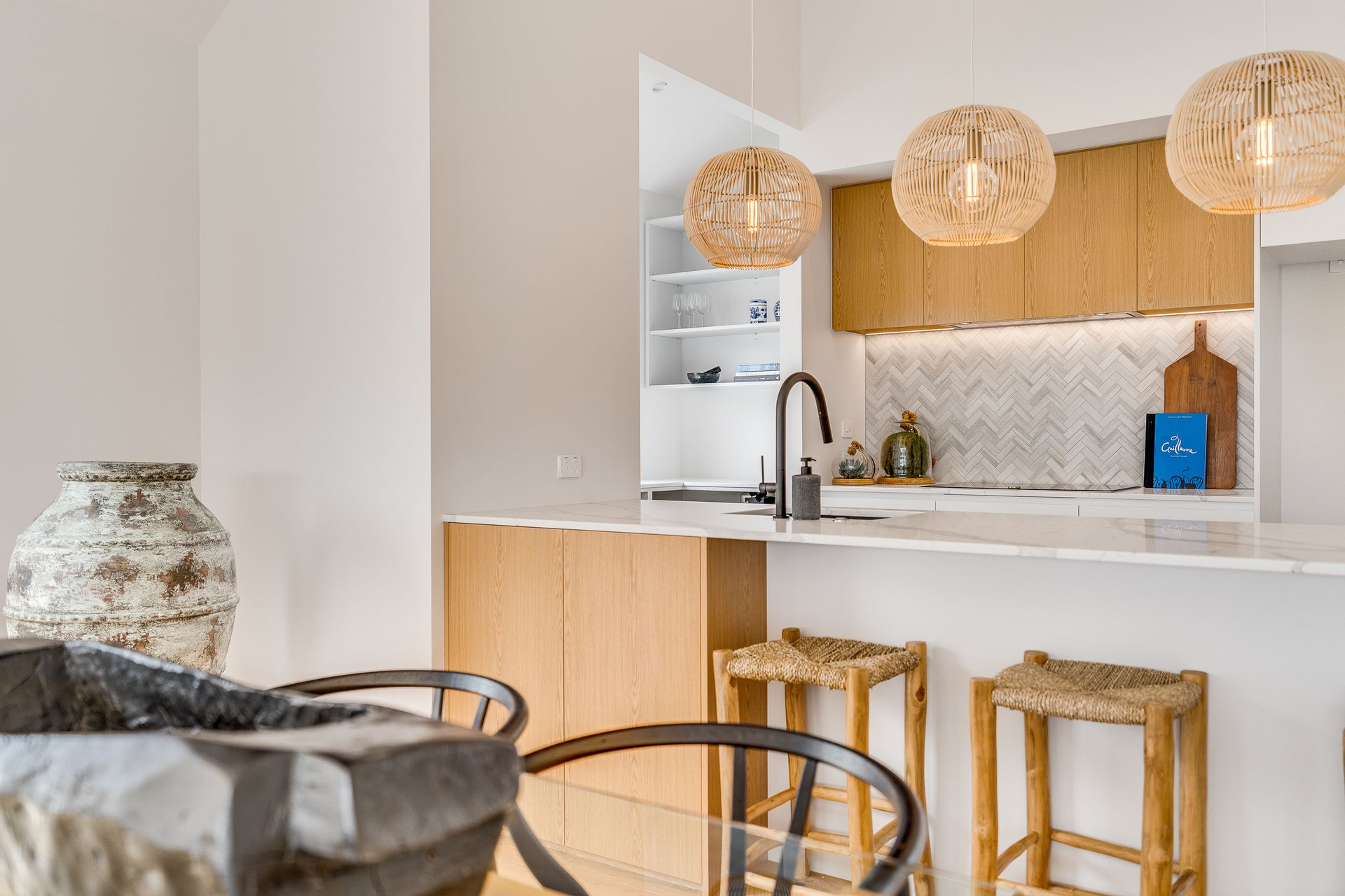 A kitchen with a table , chairs , stools and a vase on the counter.