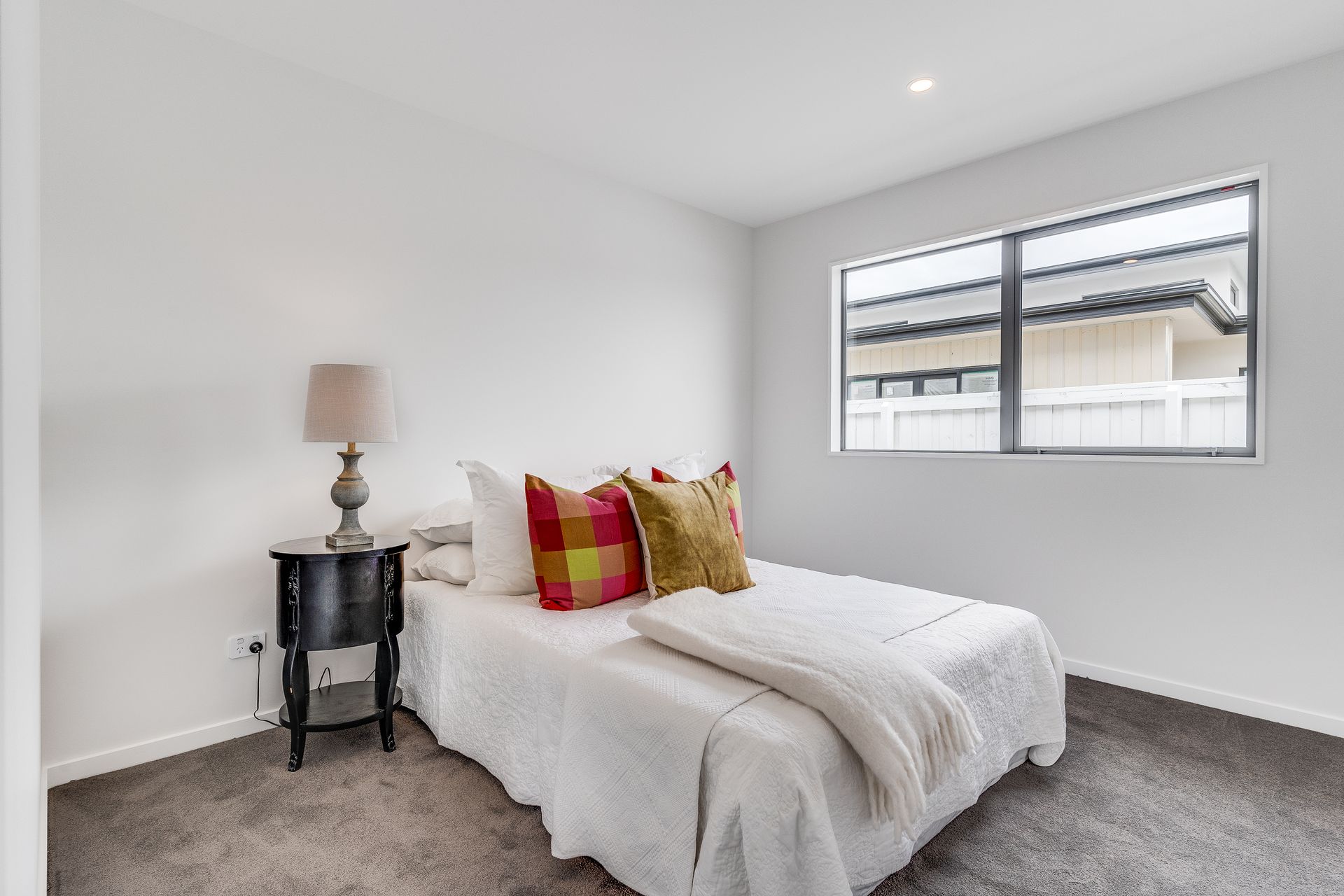 A bedroom with a bed , nightstand , lamp and window.
