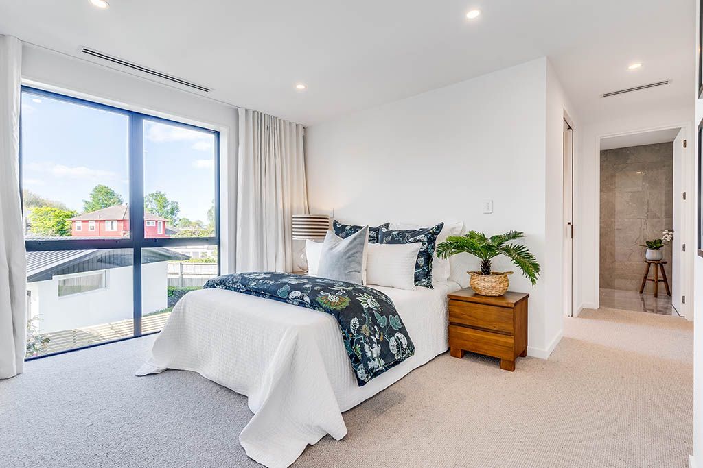 A bedroom with a bed , nightstand , and large windows.
