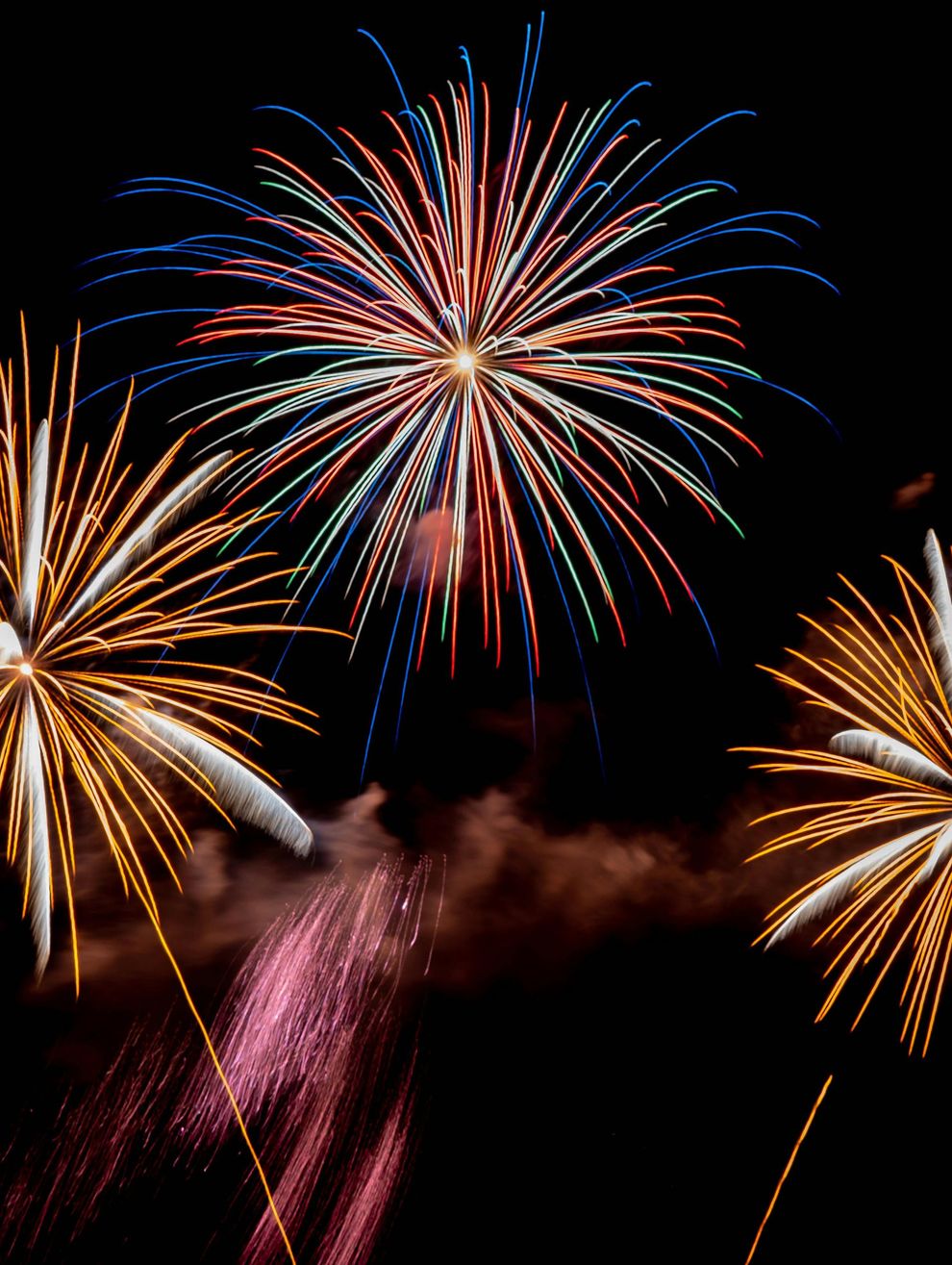 Fuochi d'artificio colorati esplodono contro un cielo notturno scuro sopra una nuvola di fumo
