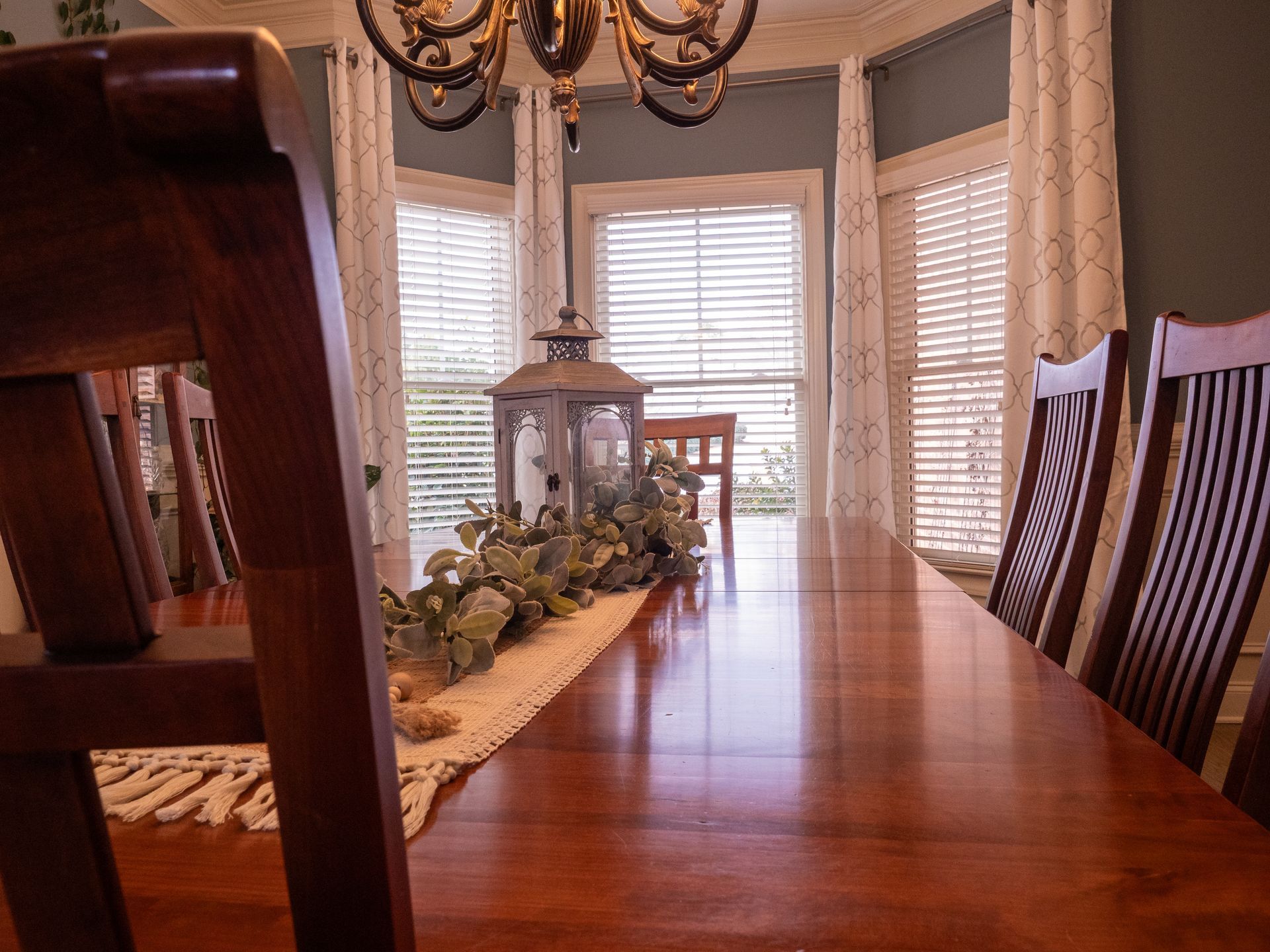 Polished and shined dining room table with boho centerpiece showing bay windows with white curtains