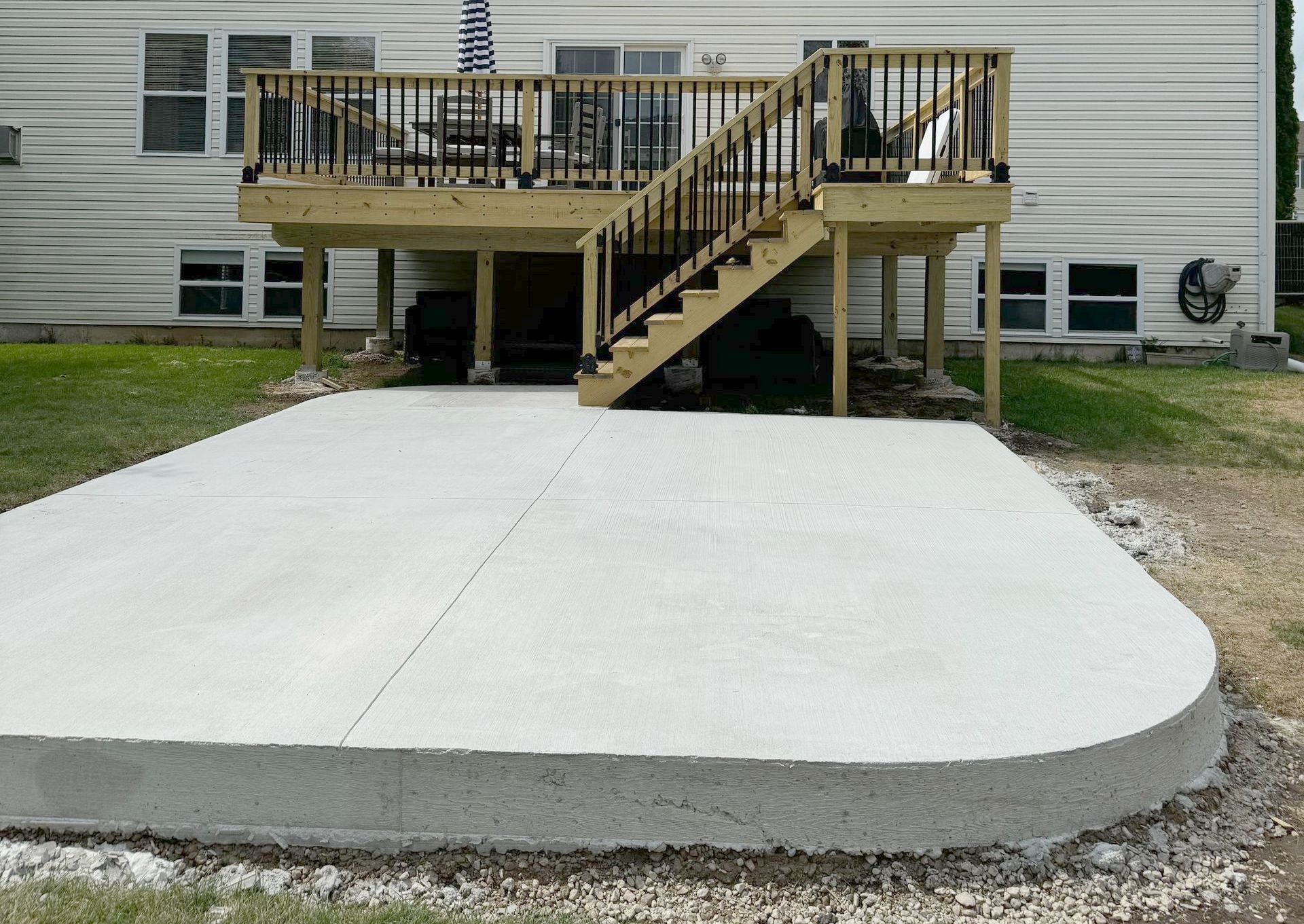 A concrete patio with a wooden deck and stairs