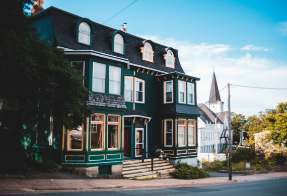 A large green house is sitting on the corner of a street.