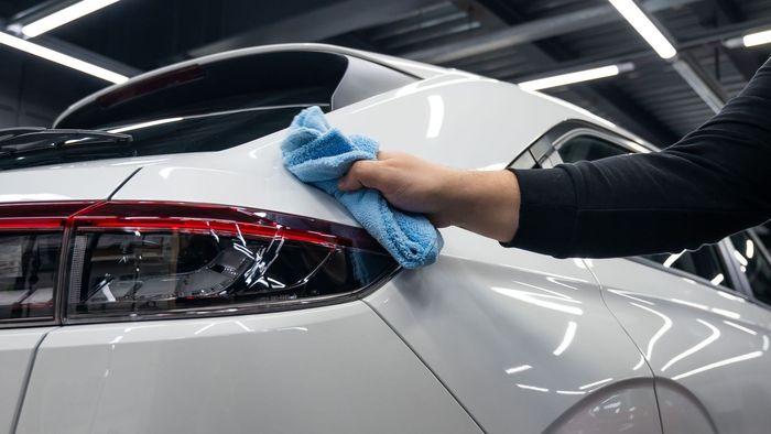 A person is cleaning a white car with a blue towel.