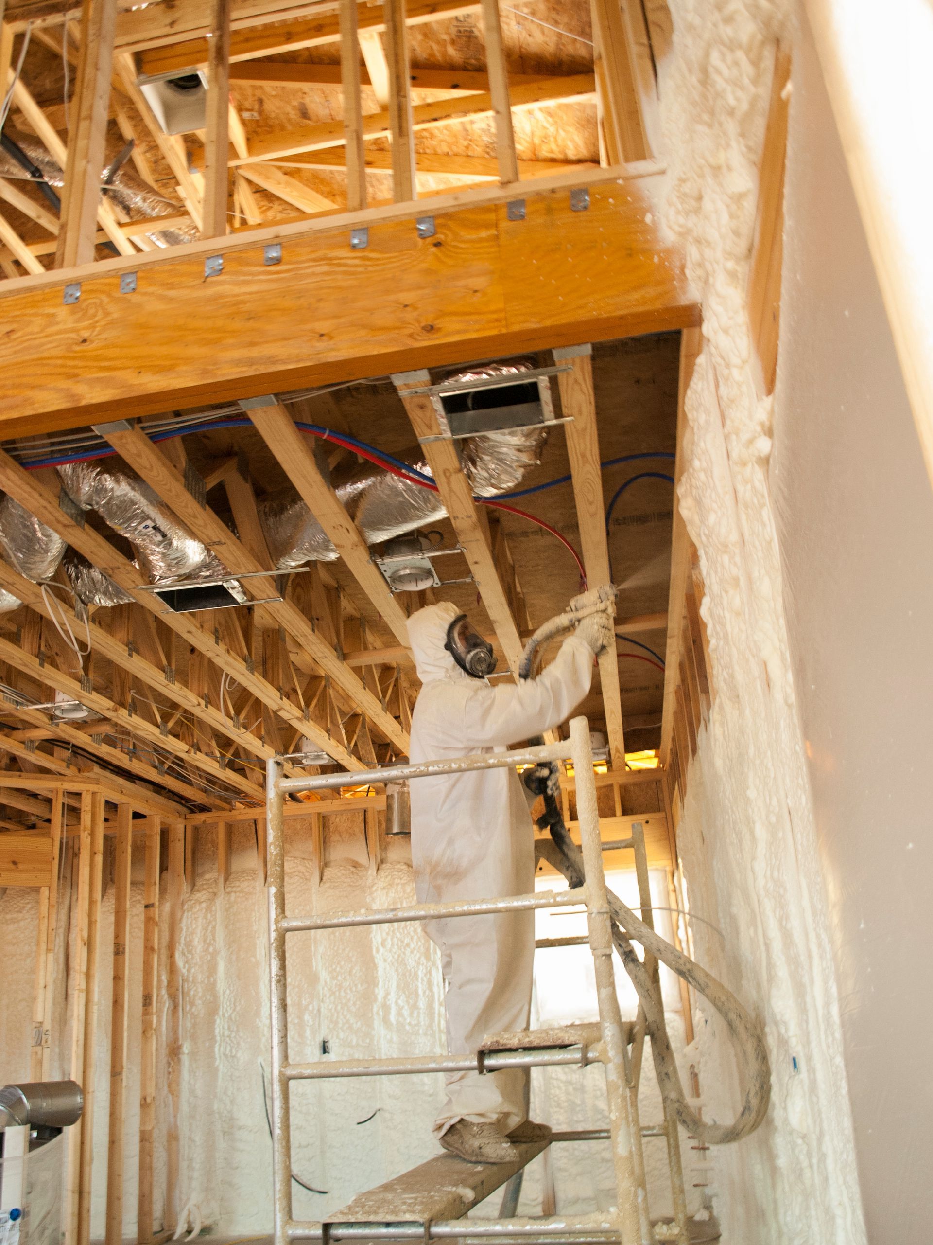 A man is spraying foam on a wall in a house under construction.