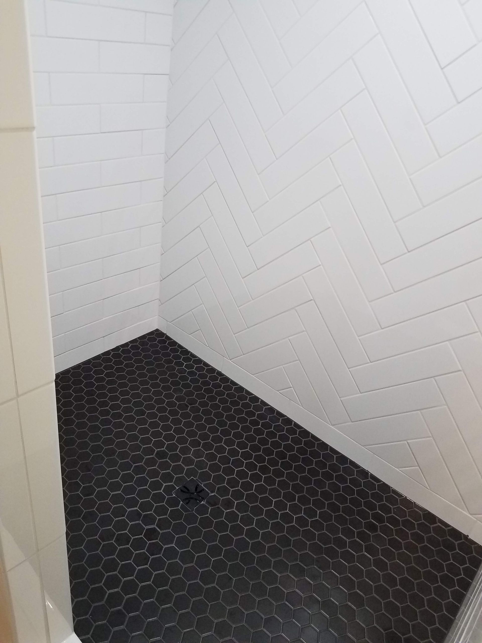Shower with black hexagonal floor tiles and white herringbone wall tiles.