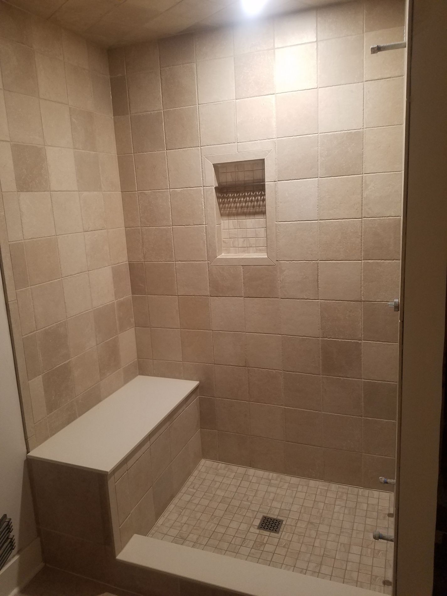 Shower with beige tile walls, bench, and pebble floor. Recessed shelf.