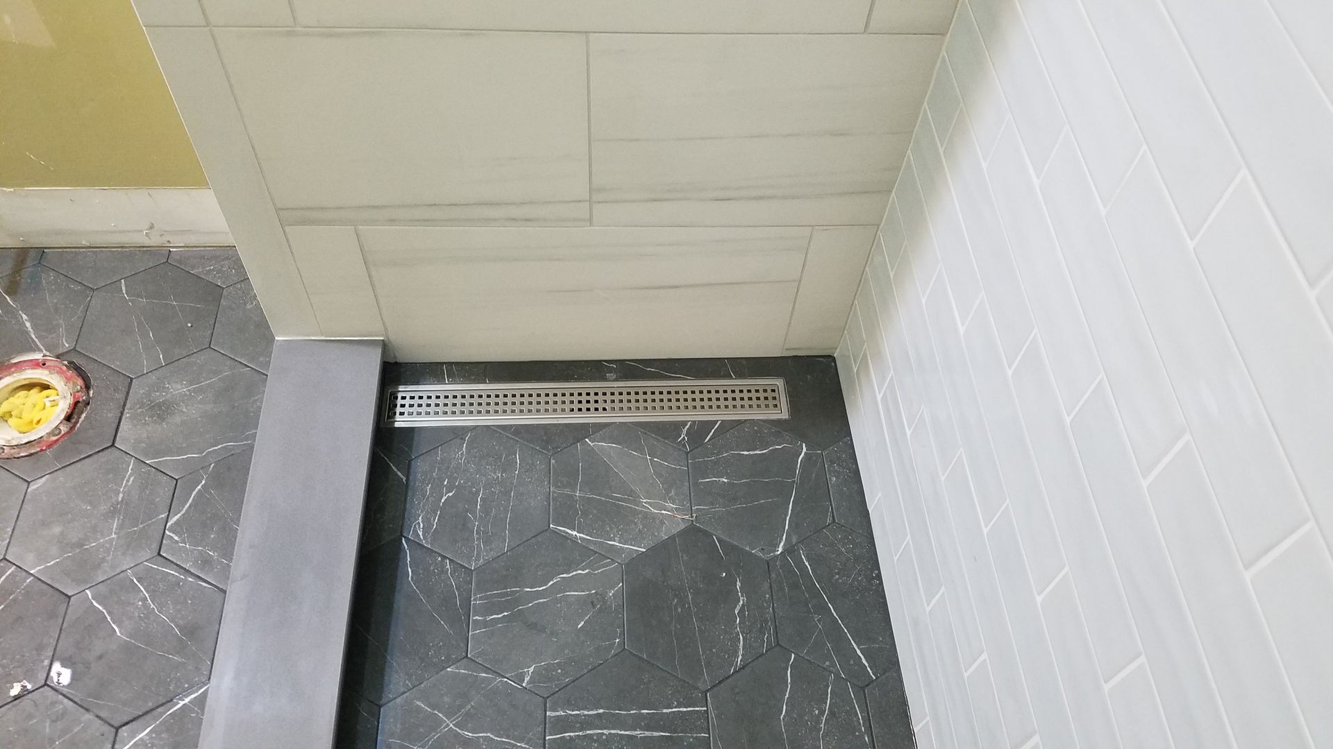 Shower with linear drain and dark stone wall, light tile walls and ceiling.