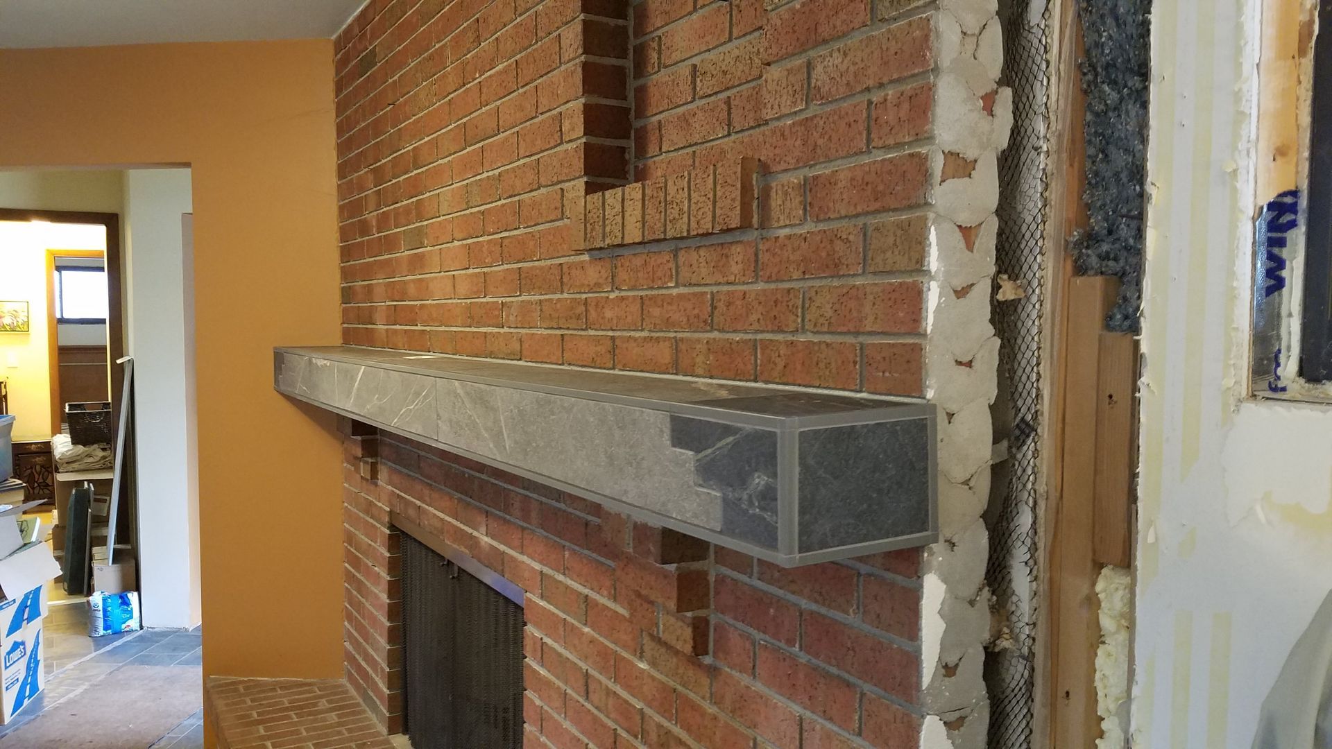 Brick fireplace with gray stone mantle. A wall is being renovated next to the brick.